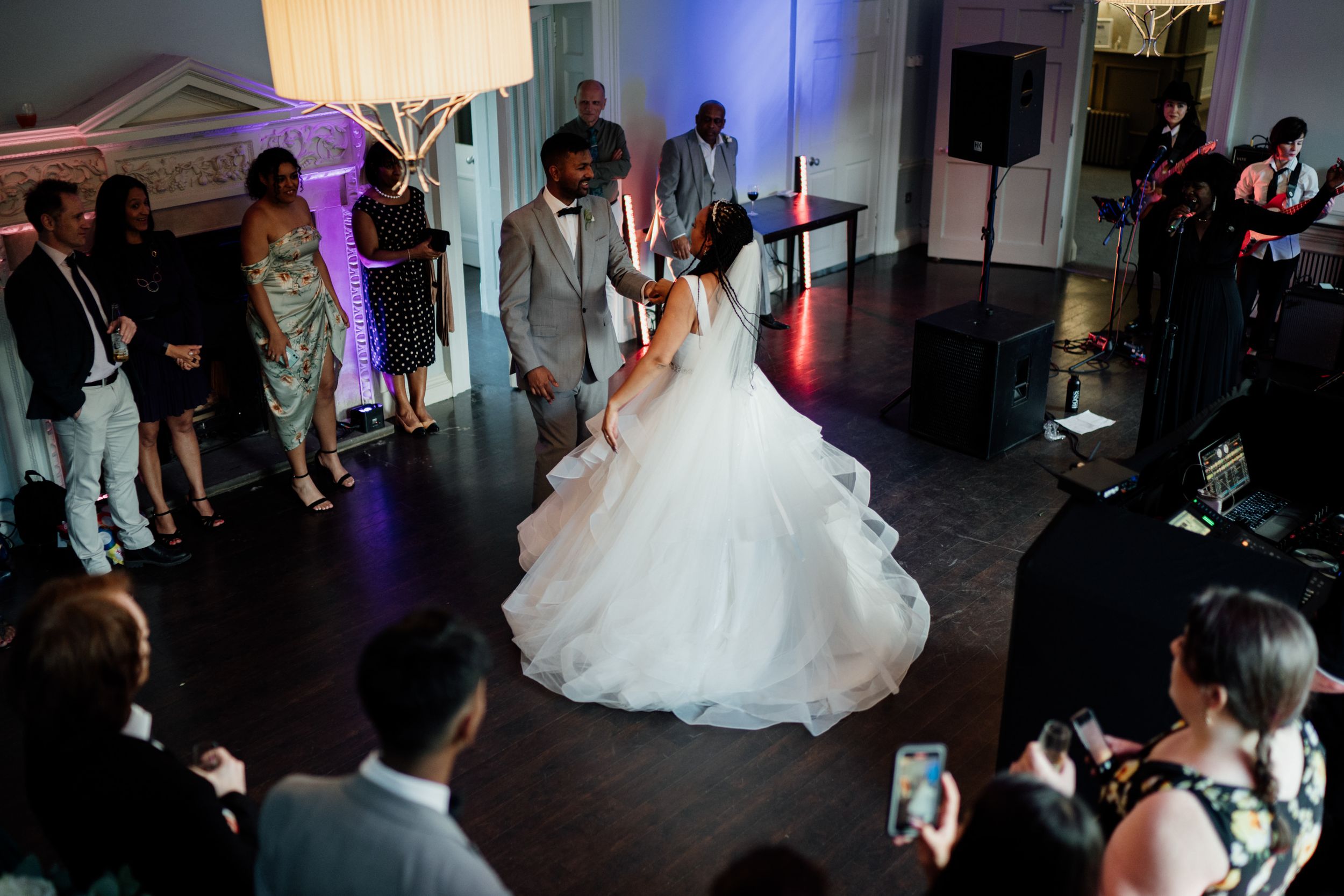 Dancing couple at a wedding reception at Morden Hall with guests watching and taking photos on a dark dance floor with purple lighting.