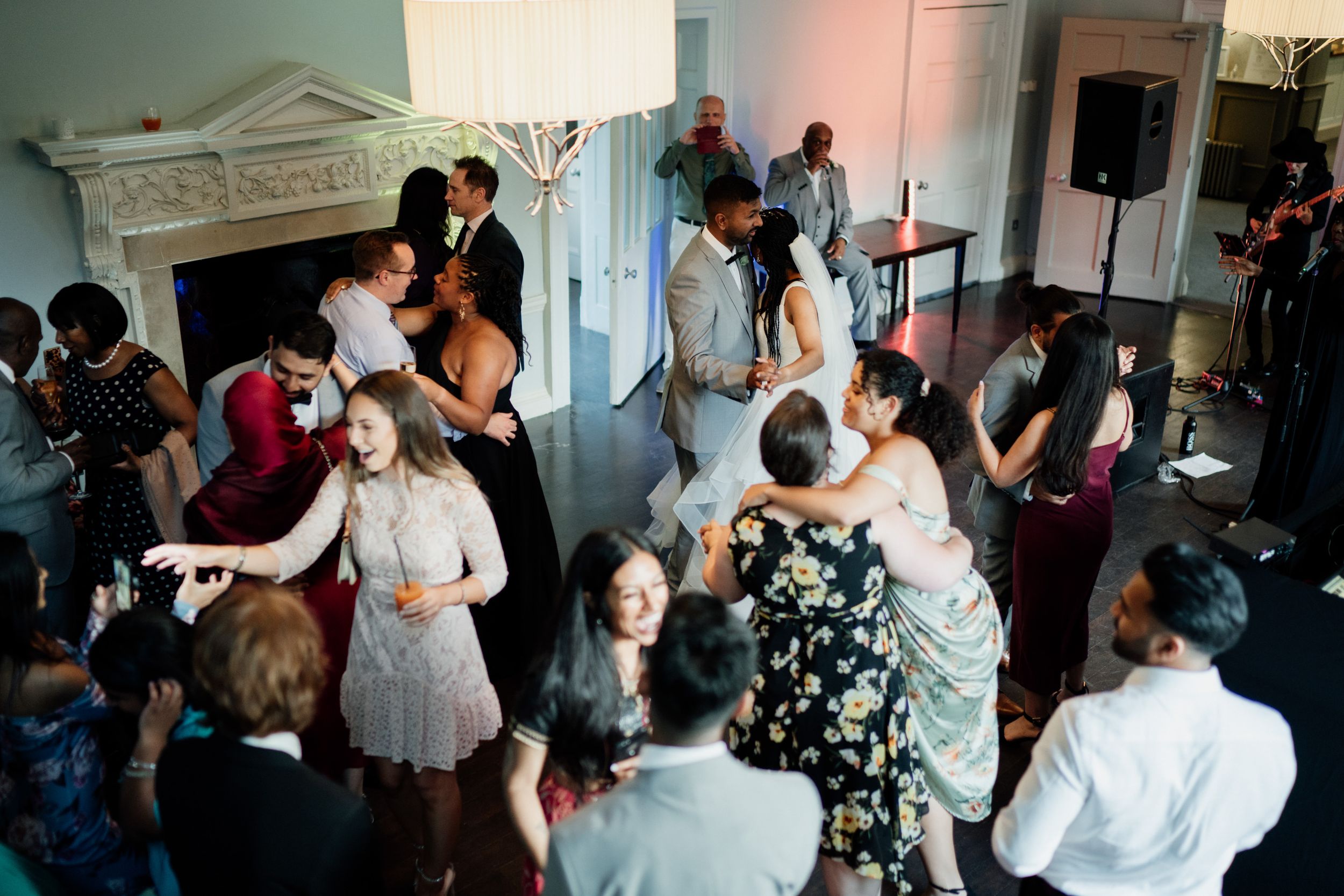A group of people dancing and socializing at an indoor party with live music near an ornate fireplace mantel.
