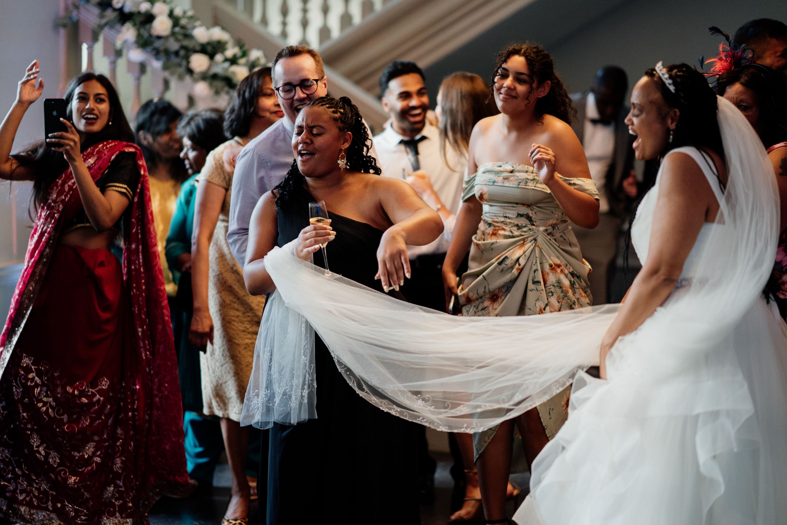 Wedding guests dance and celebrate with the bride's flowing white dress during a joyful reception moment.