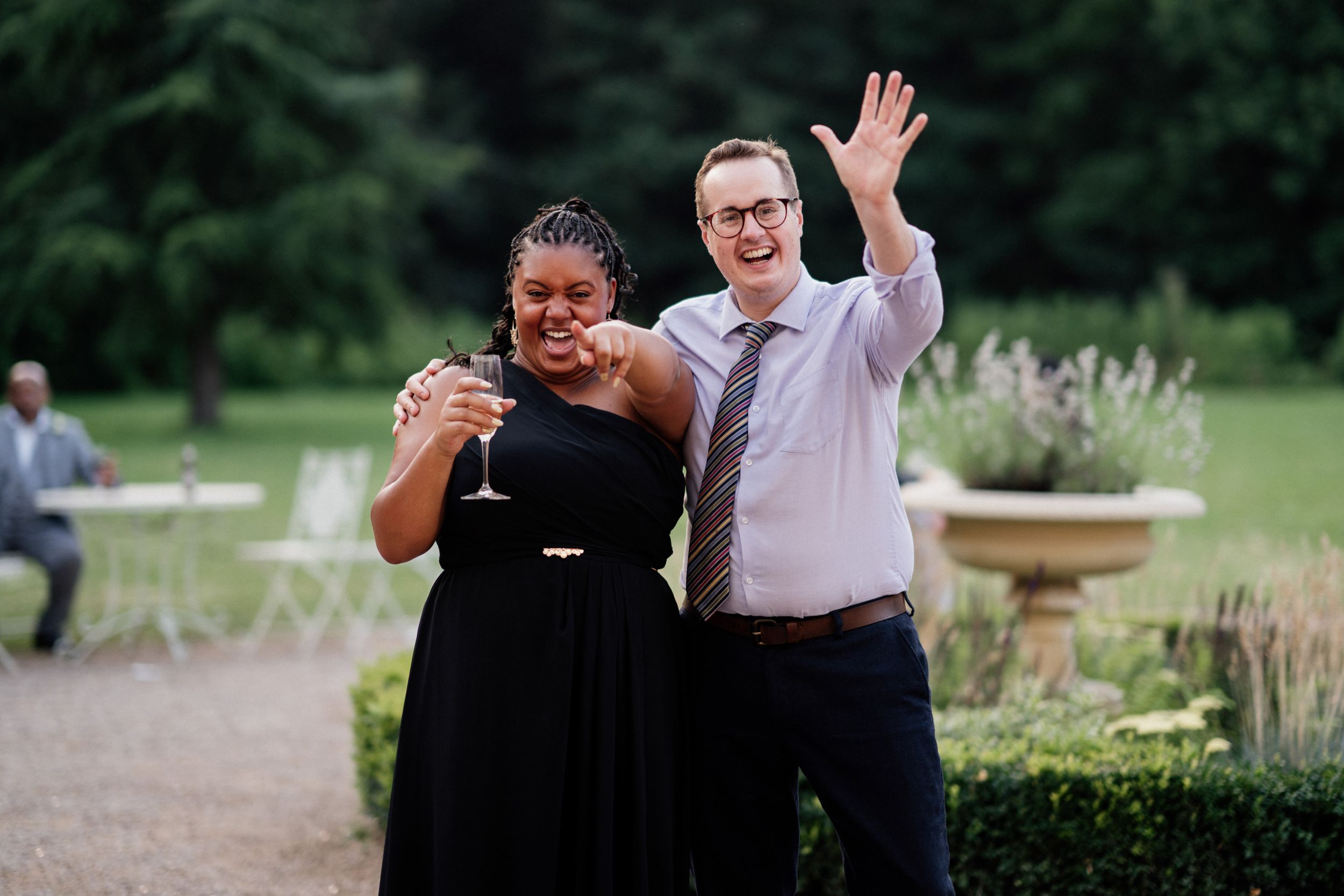 Two people sharing a joyful moment at a garden wedding with one laughing and one waving.
