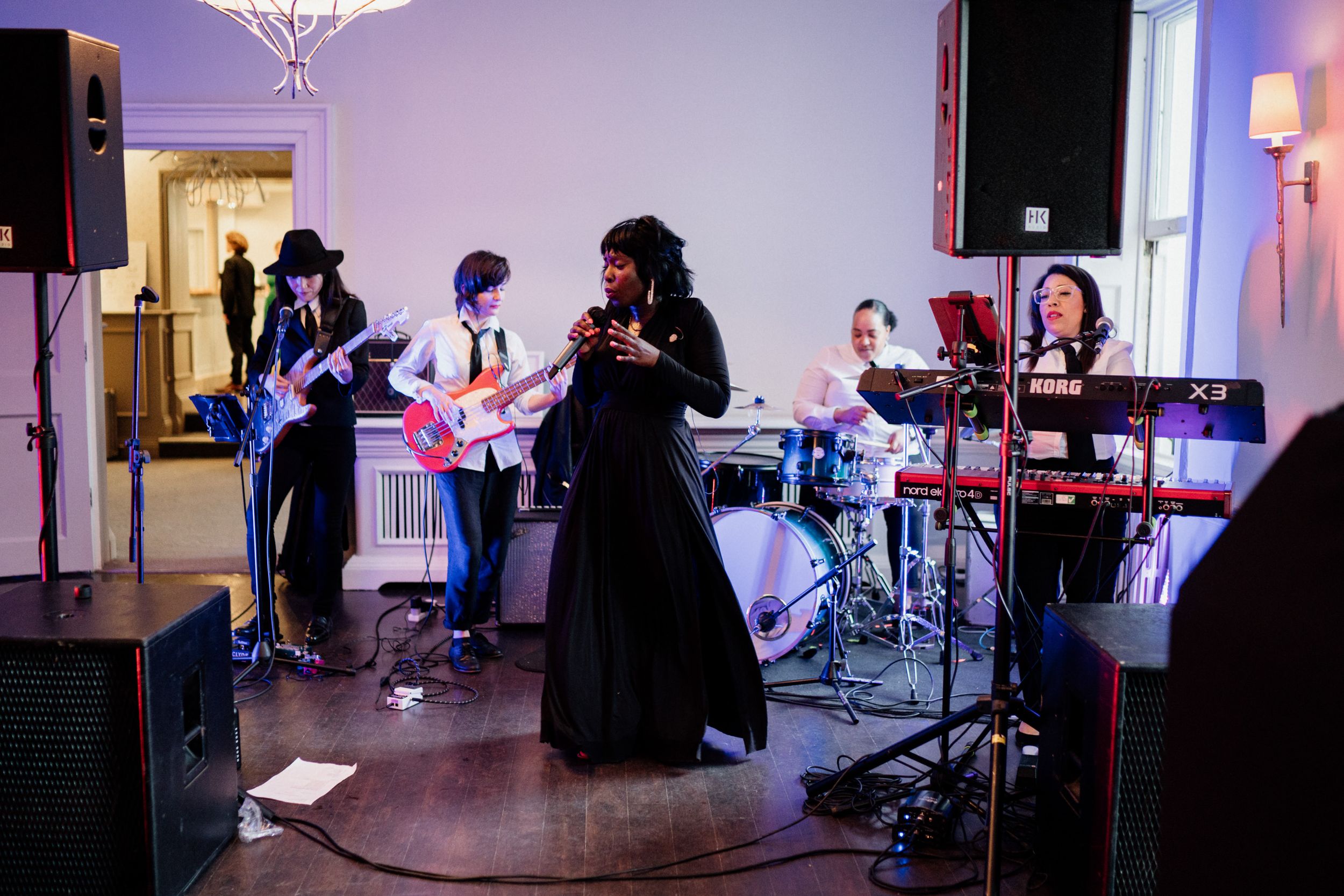 Live band performs on stage at an indoor venue with purple lighting and a singer in a black dress at the microphone.