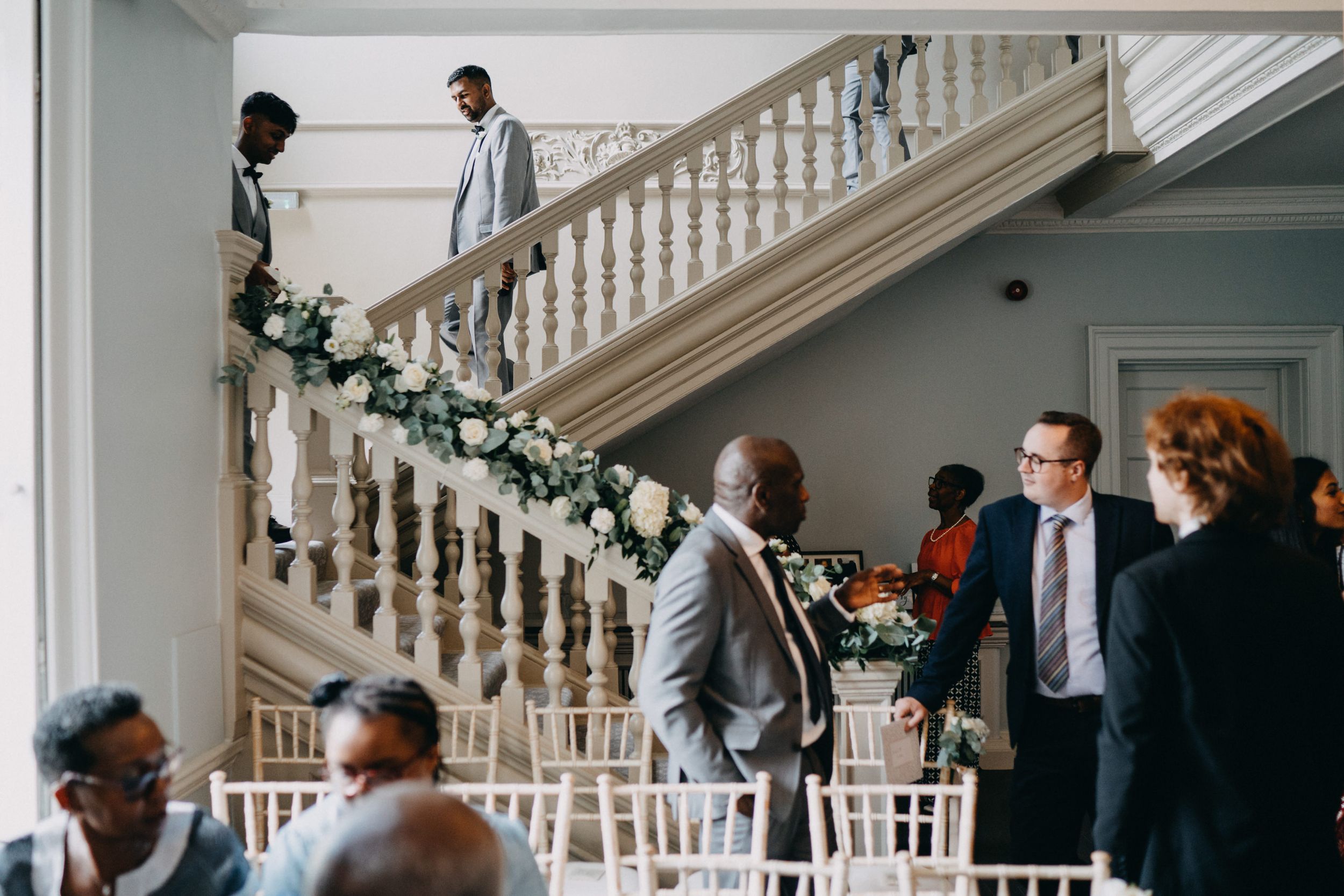 Interior of an elegant venue with a decorated staircase and guests mingling during an event.