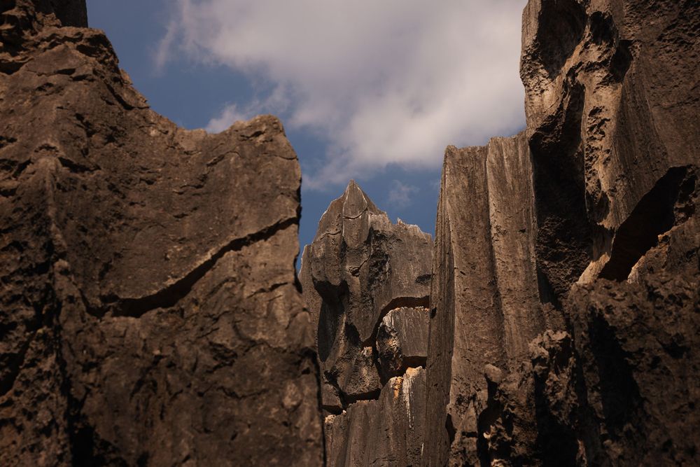 Dramatic rocky cliffs and jagged mountain peaks rise against a cloudy blue sky in a rugged wilderness landscape.
