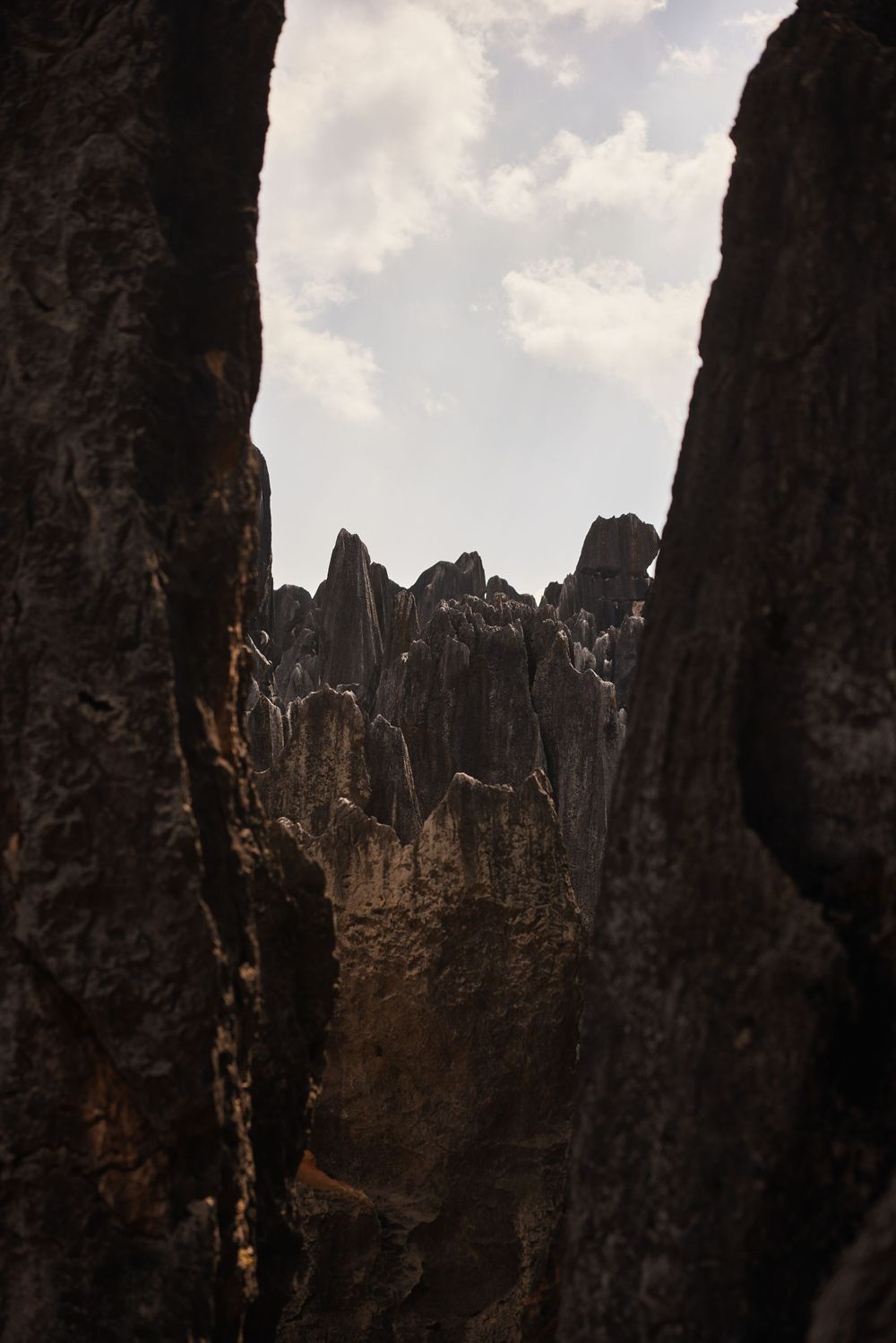 Jagged mountain peaks rise dramatically between dark rocky cliffs under a cloudy sky in a dramatic landscape view.