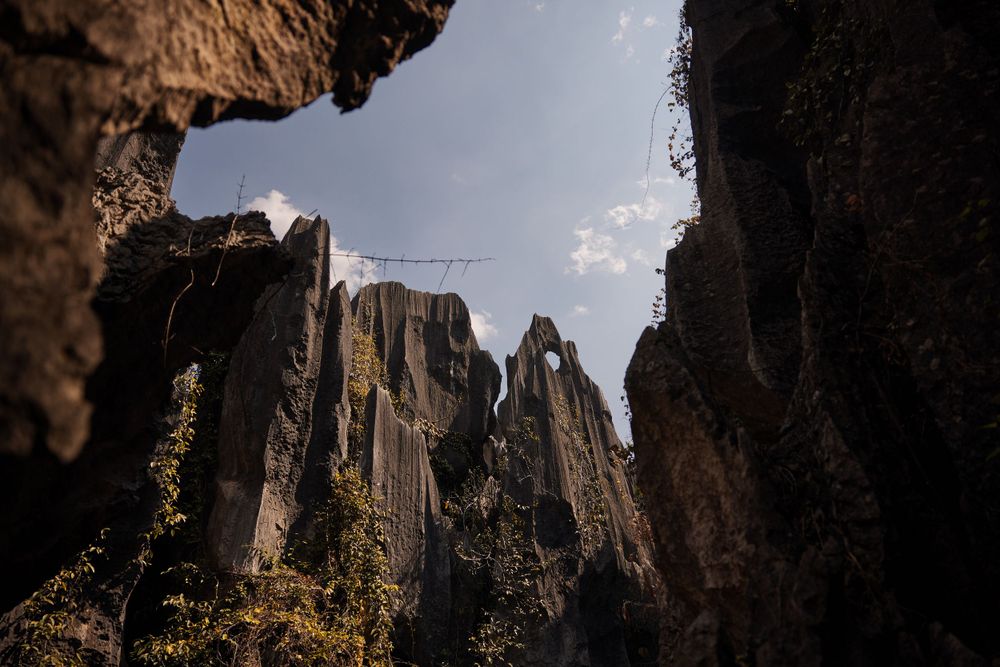 Dramatic view of tall rocky spires and cliffs framed through a natural stone arch against a misty sky.