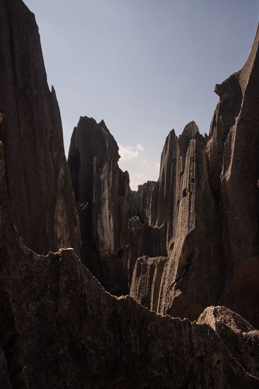 Dramatic jagged rock formations rise against a bright sky creating dramatic shadows in a mountainous landscape.