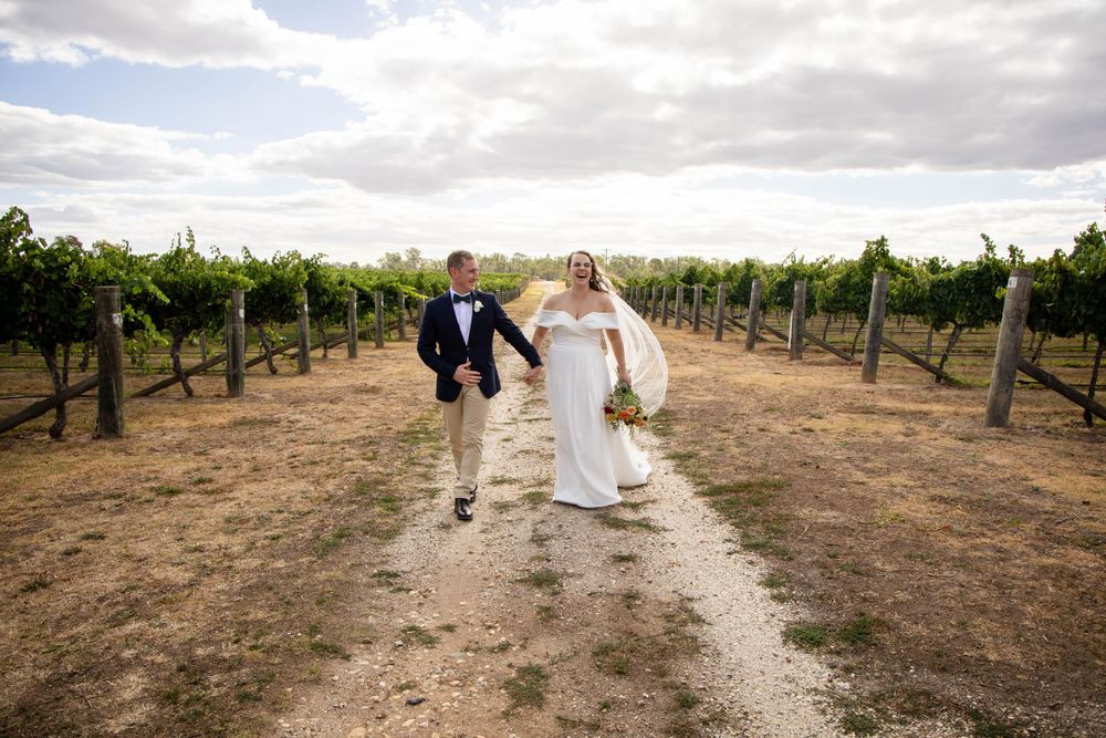 A couple walks hand in hand between rows of grapevines at a vineyard on their wedding day.