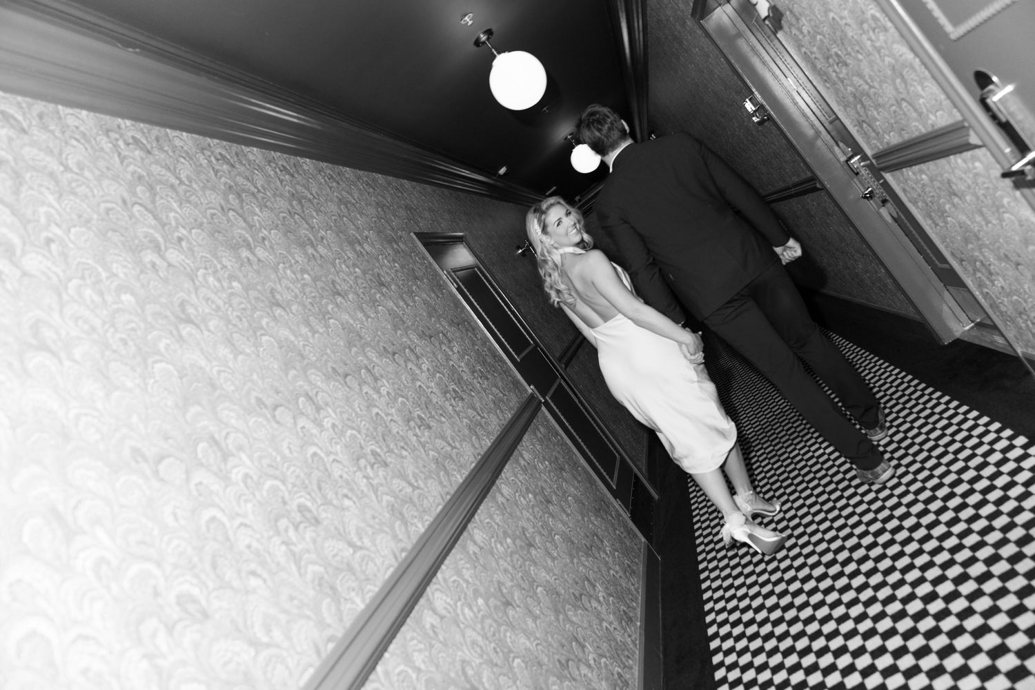 A black and white photo of dancers in a long hallway with geometric flooring. Engagement Session at The Lafayette Hotel in San Diego. JPPC