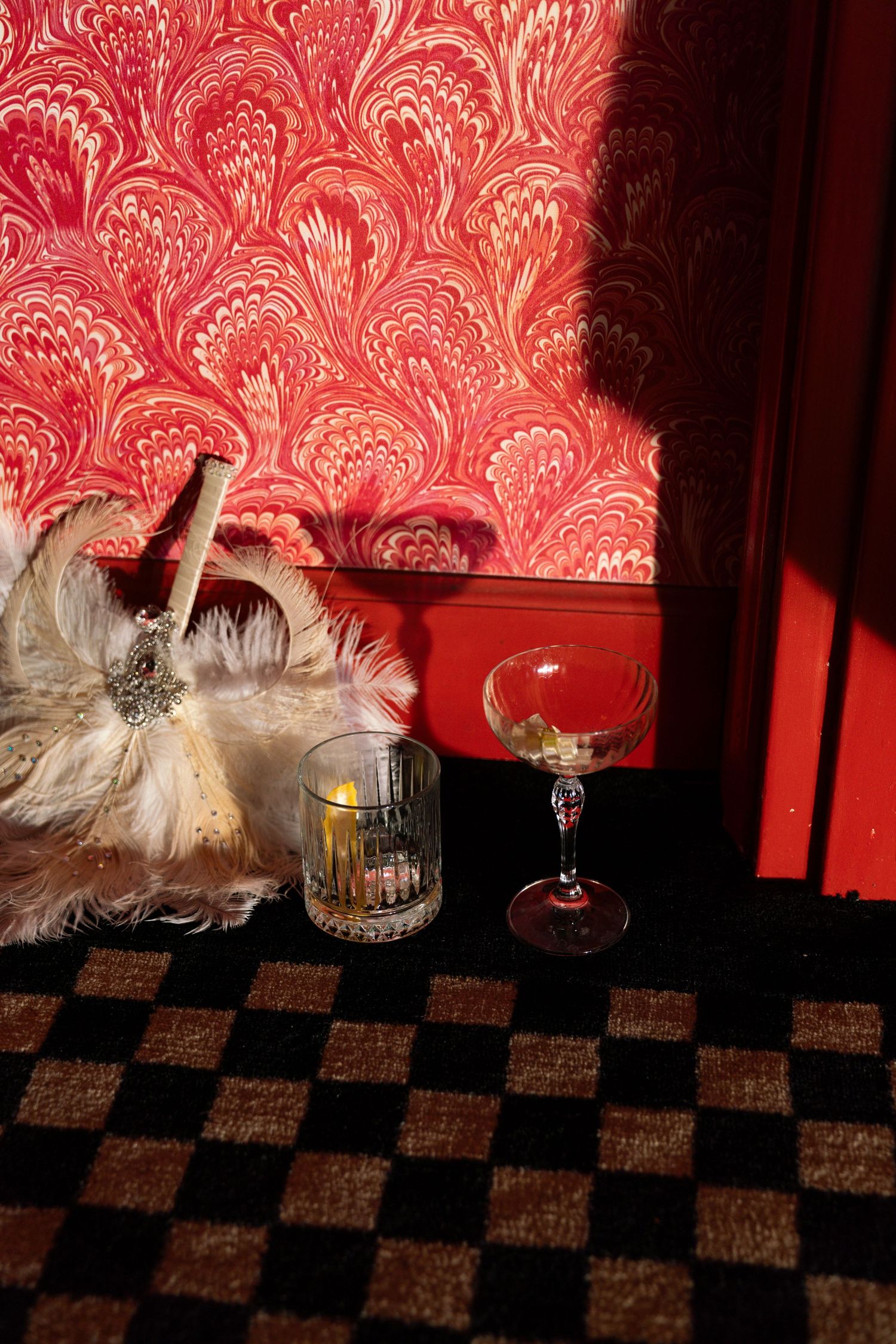 Decorative drinks setup with feathers and glasses against red damask wallpaper and checkered floor. Engagement Session at The Lafayette JPPC