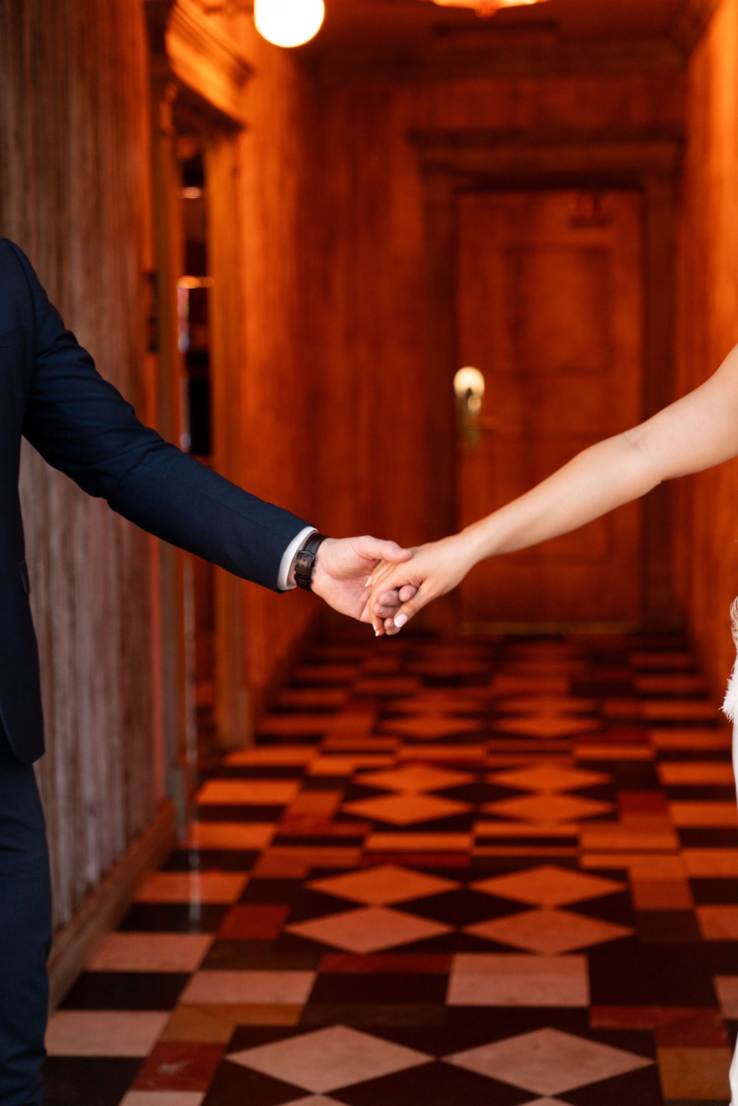 Two people holding hands romantically in a hallway with a geometric patterned floor and warm lighting. Jessica Paige Photo Co. Best Wedding