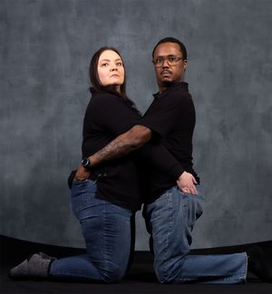 Artistic studio portrait of two people kneeling in matching black tops and jeans.