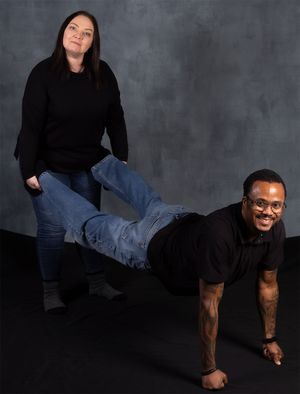 Playful studio photo with one person doing a plank pose while another stands beside them.