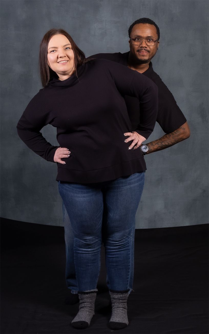 Studio portrait of a couple in black sweaters against a dark gray backdrop.