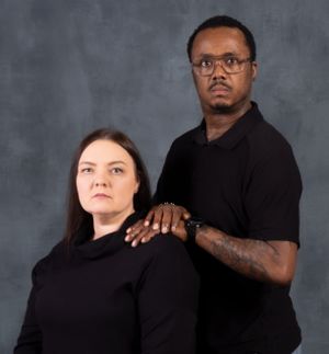 Studio portrait of couple in black tops against gray background with dramatic lighting.