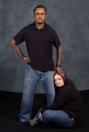 Creative studio portrait with one person standing while other sits low in frame.