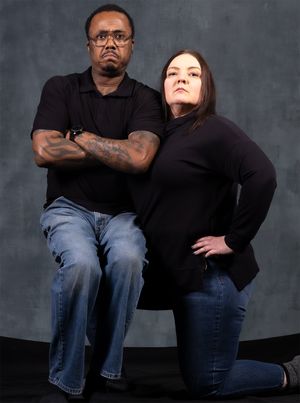Two people in matching black tops strike a confident posed stance against gray background.