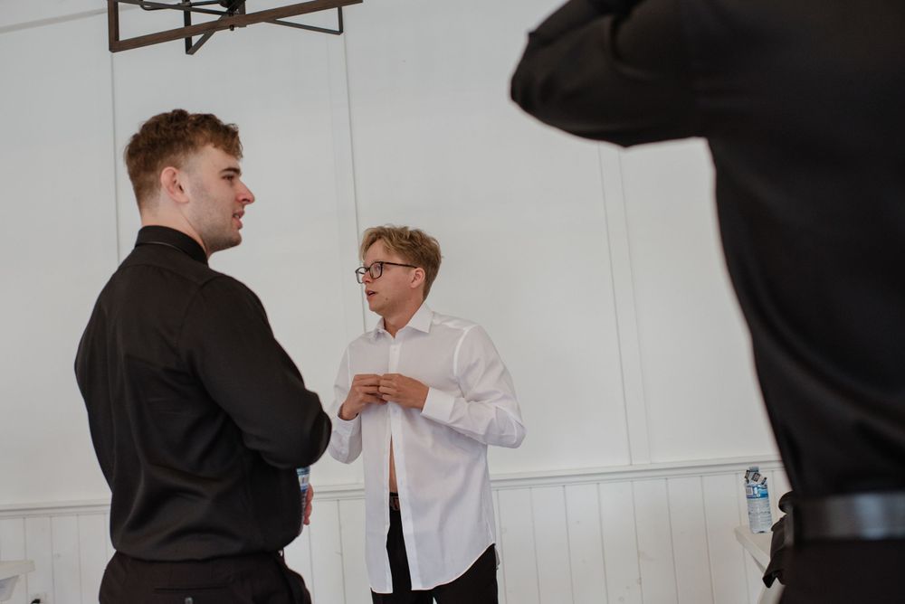 Two people having a conversation in a bright white room near a coat rack.