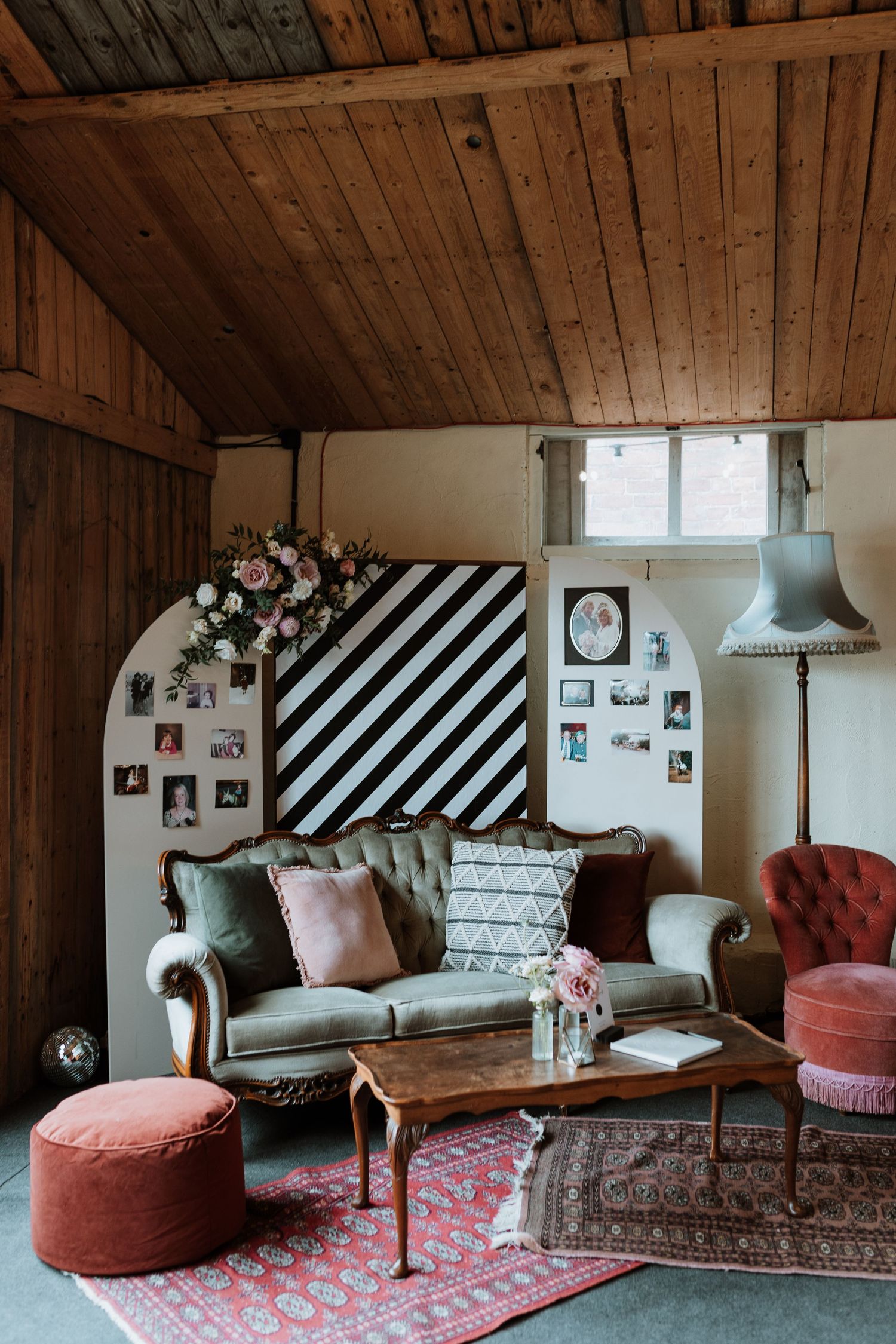 Cozy living room with vintage sofa, striped accent wall, pink ottoman and oriental rug under wooden beam ceiling.
