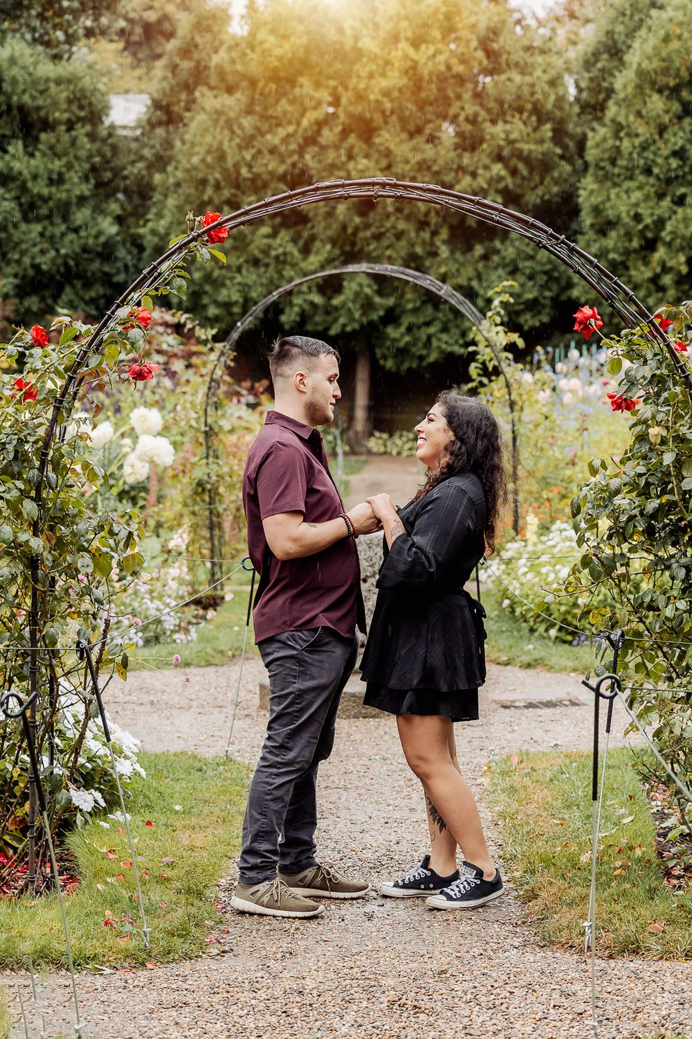 A couple holding hands under a floral garden arch with red and white roses.
