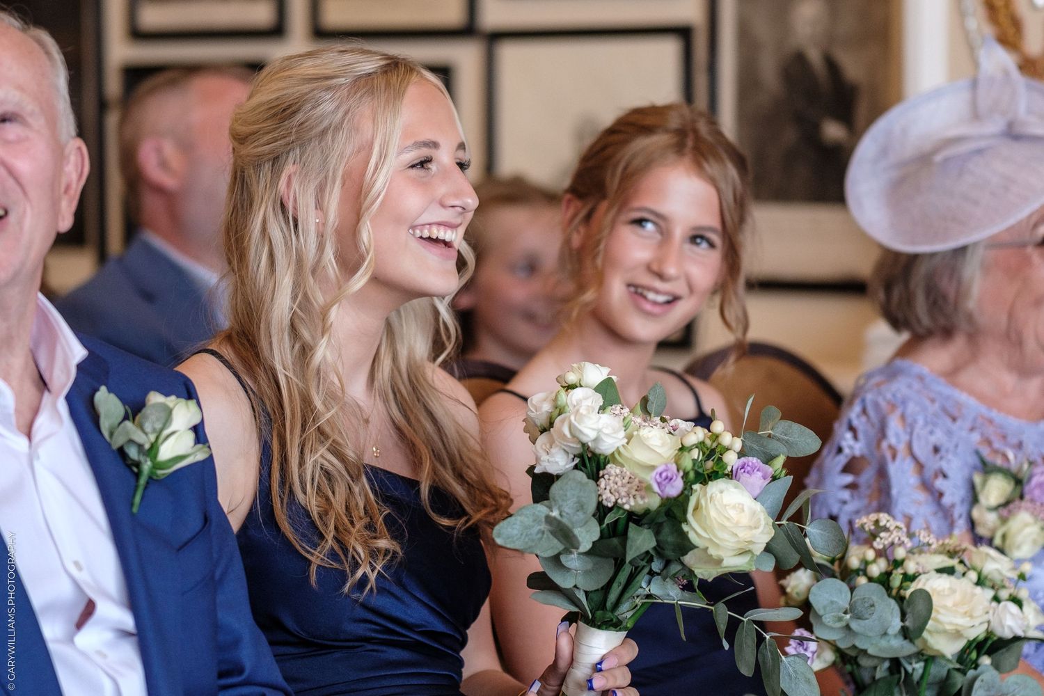Wedding guests share joyful laughter while holding elegant white rose bouquets at formal celebration.