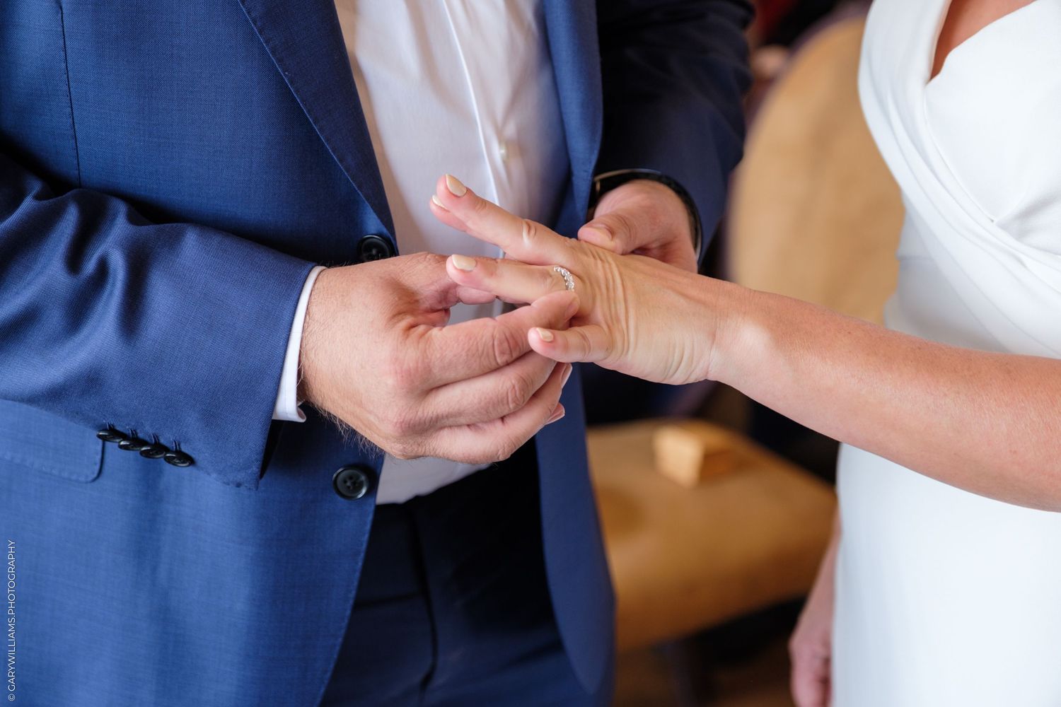 Close-up shot of hands exchanging wedding rings during marriage ceremony with groom wearing navy blue suit.