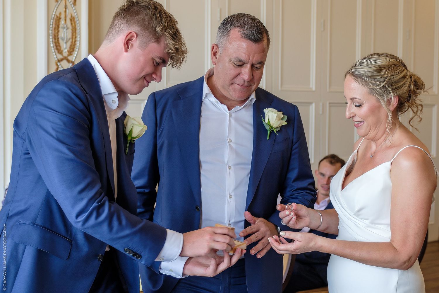 A wedding ceremony moment shows the exchange of rings with the officiant in a light-colored room.
