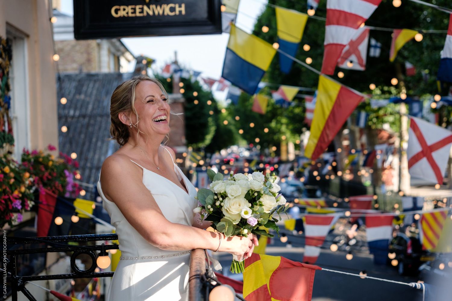 Bride and groom dance under vibrant flag decorations at an outdoor evening reception with string lights.
