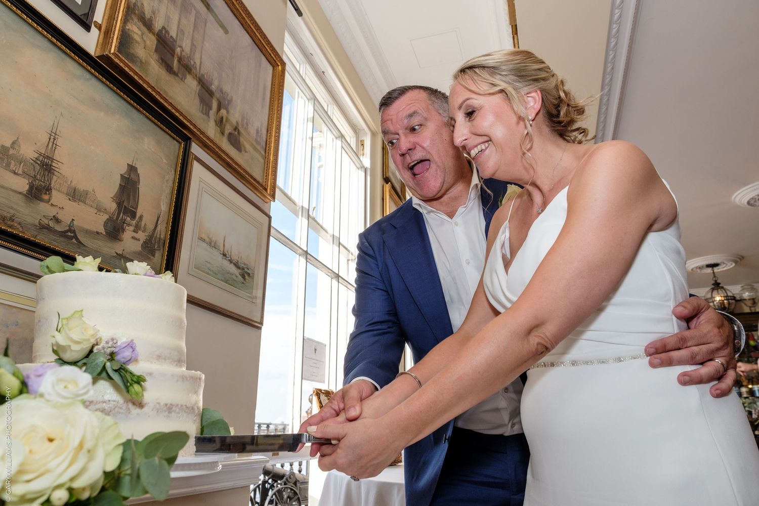 A happy couple cuts their white wedding cake together during their reception celebration.