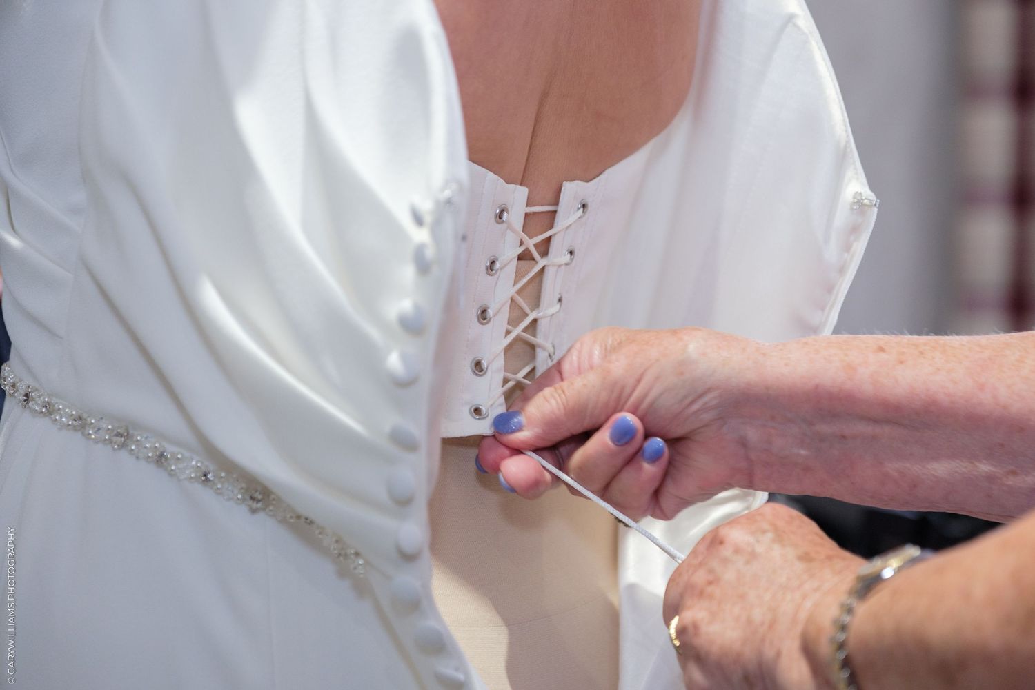 Detailed close-up showing hands threading a delicate needle with white thread through fabric.