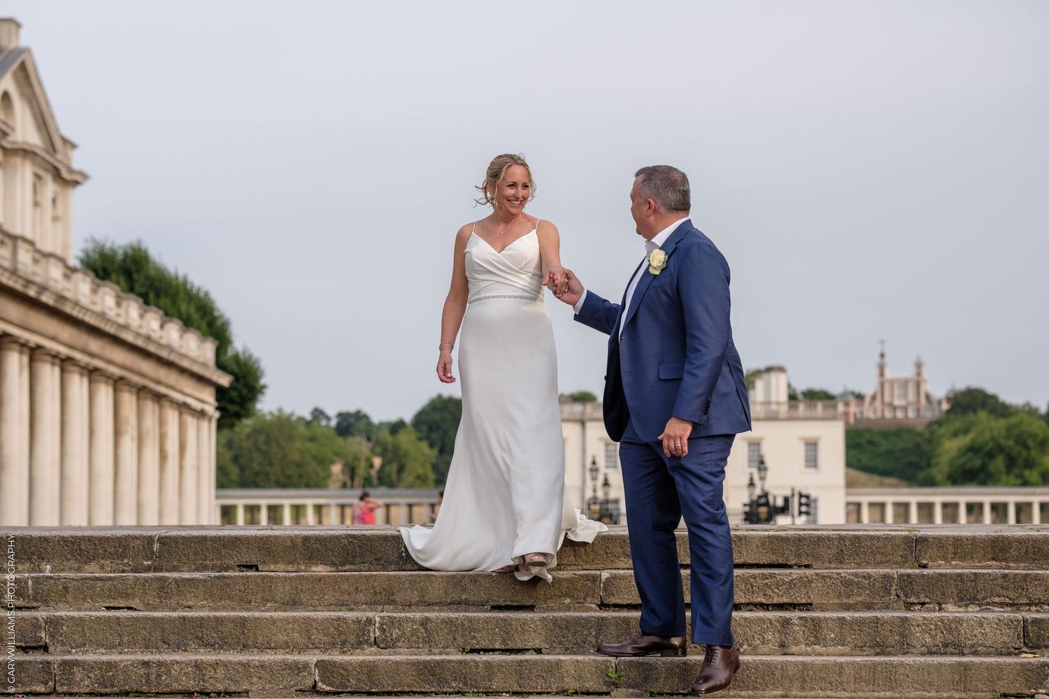 Two people in formal attire stand on historic stone steps against an elegant architectural backdrop during a wedding.