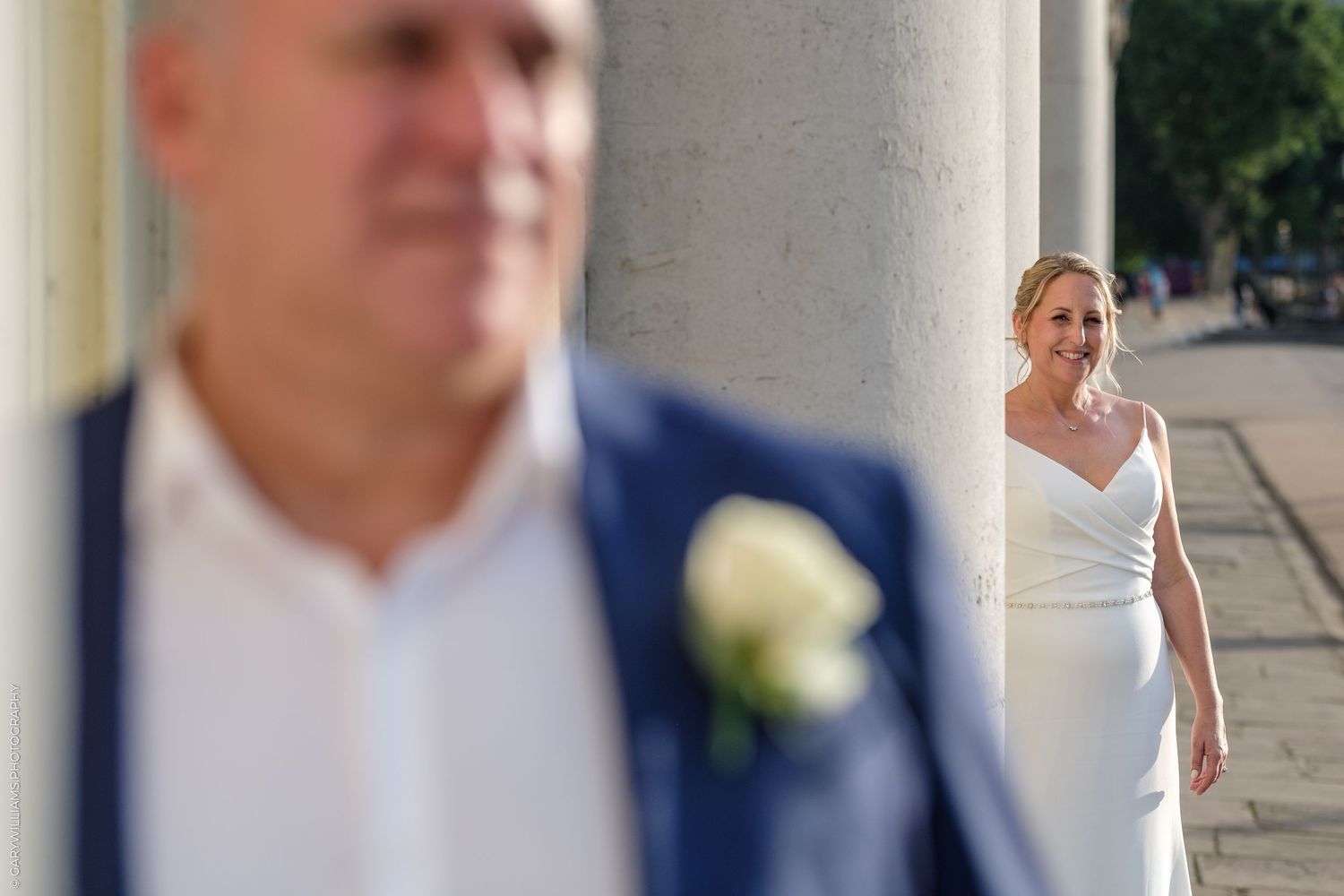 Creative wedding photo composition showing couple through stone colonnade with selective focus.