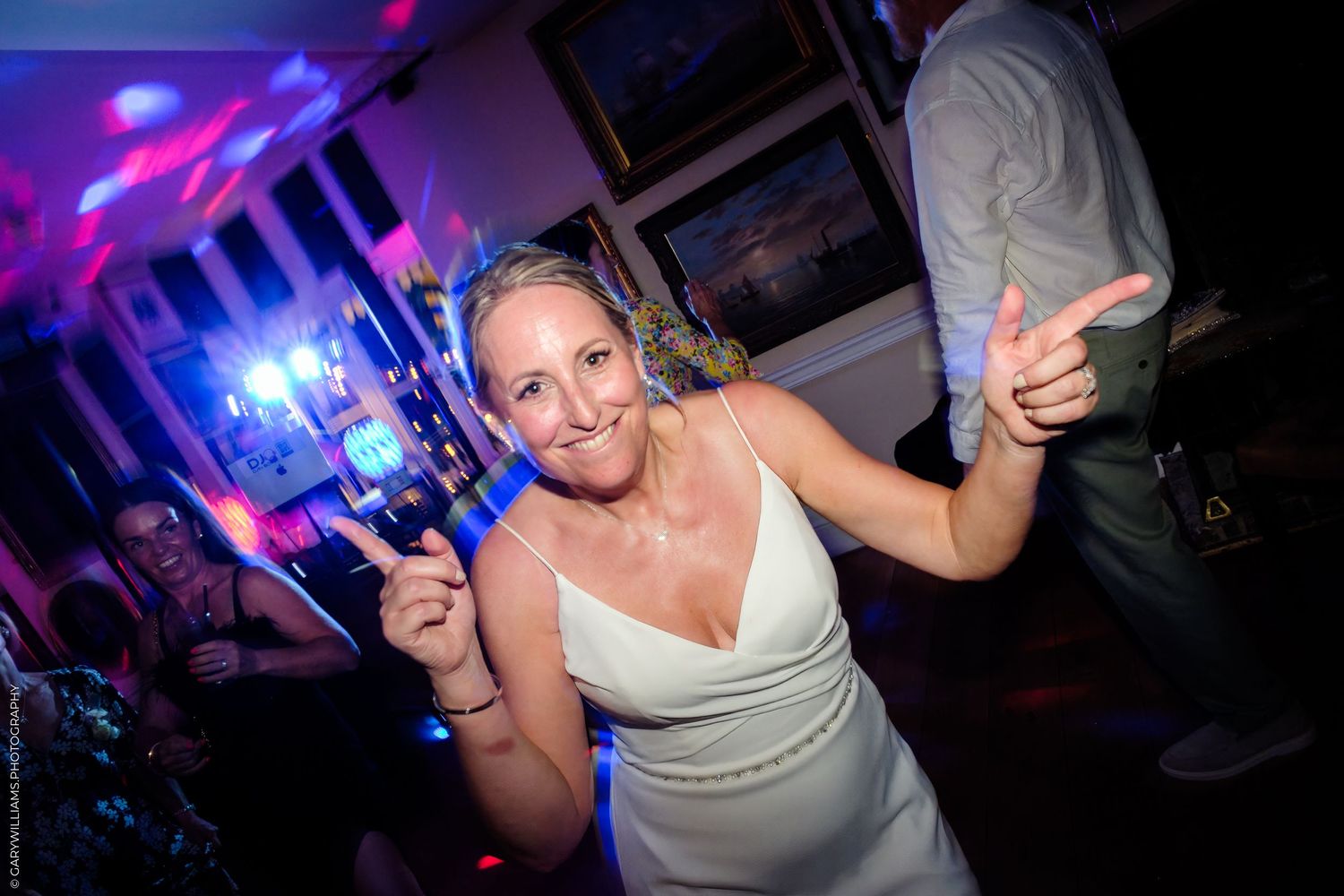 Person in white dress dances at a nightclub with colorful purple lighting and holding a drink.