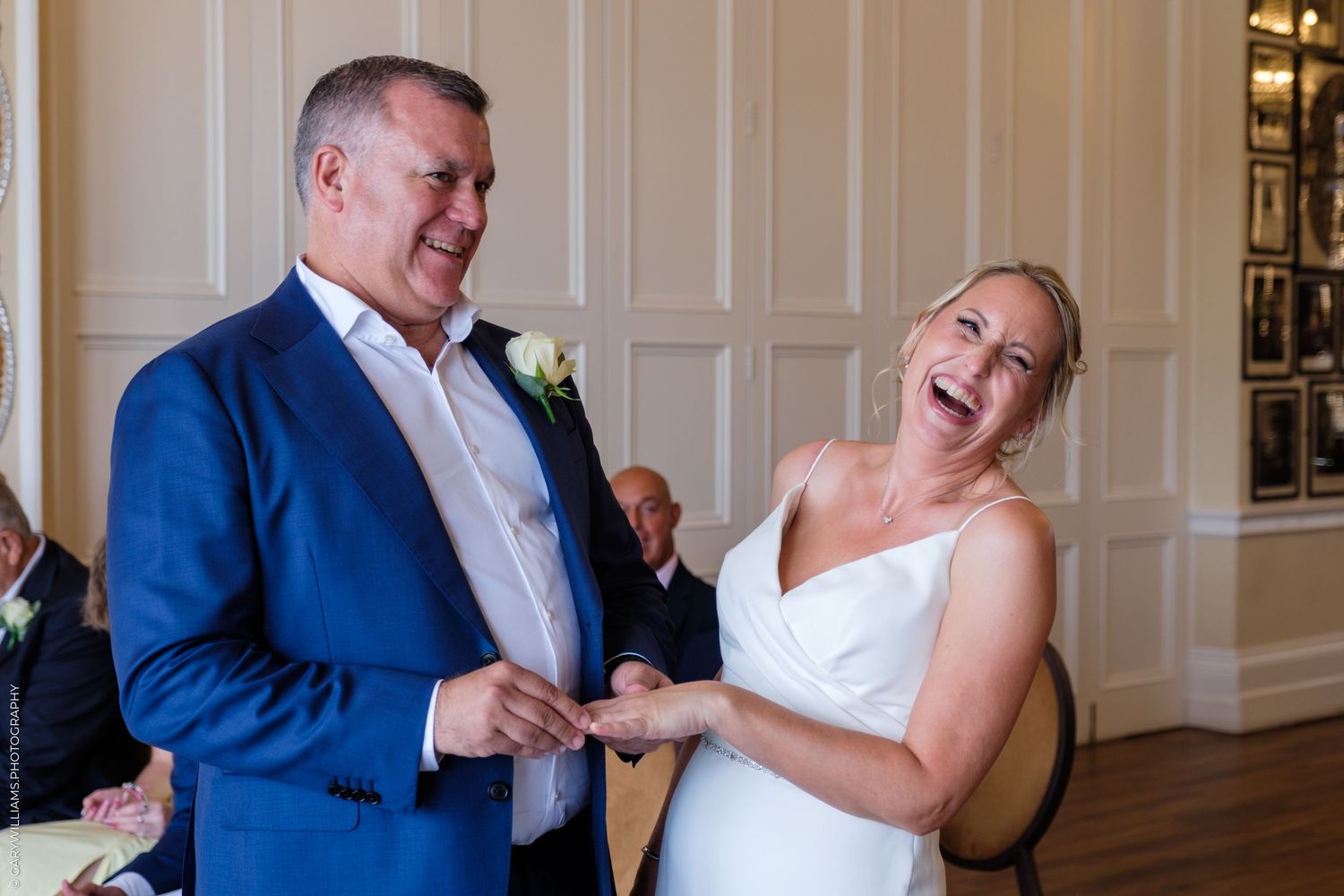 A happy couple sharing a candid laugh together during their wedding celebration in an elegant room with white paneled walls.