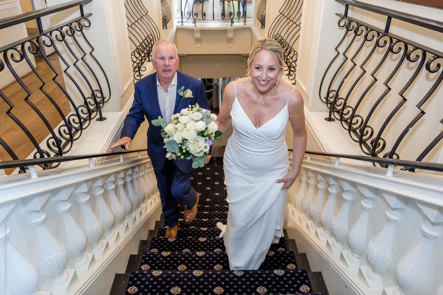 People walk together down an elegant curved marble staircase with ornate black iron railings at a formal event.