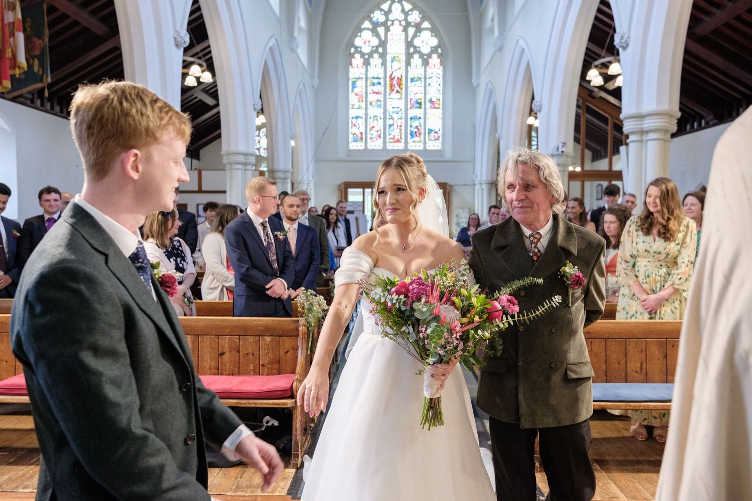 A wedding ceremony inside a beautiful historic church with stained glass windows and wooden beams on the ceiling.