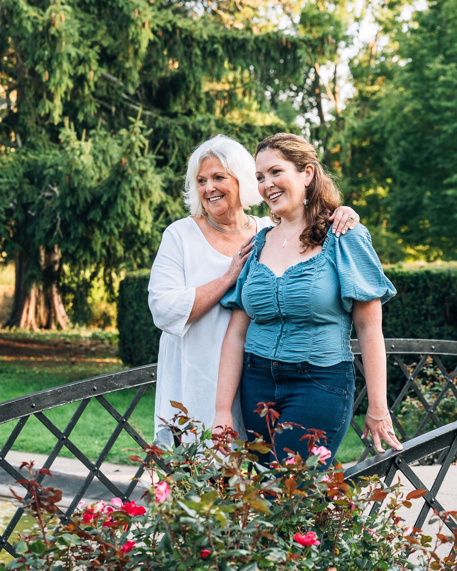 Two people standing together and smiling near a decorative railing with pink flowering plants in a garden setting.