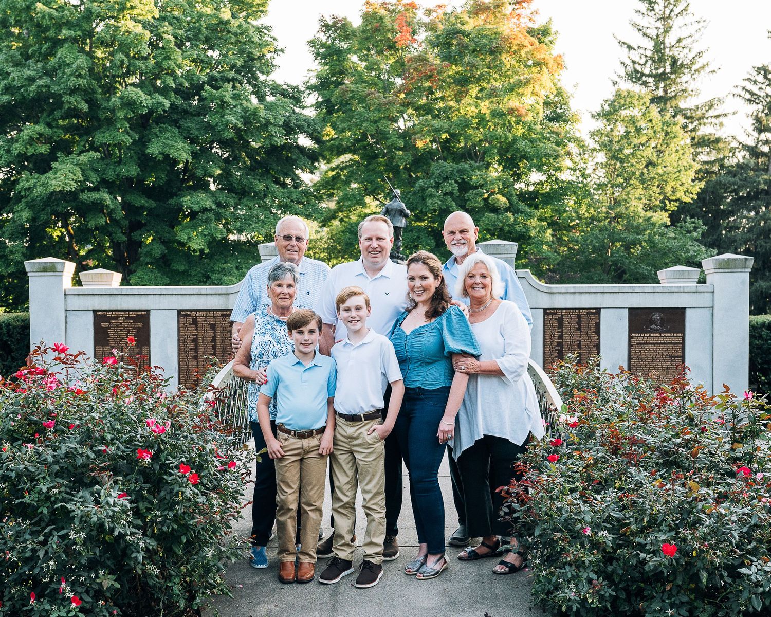 Group portrait standing together on stone patio surrounded by blooming rose bushes and autumn trees in background.