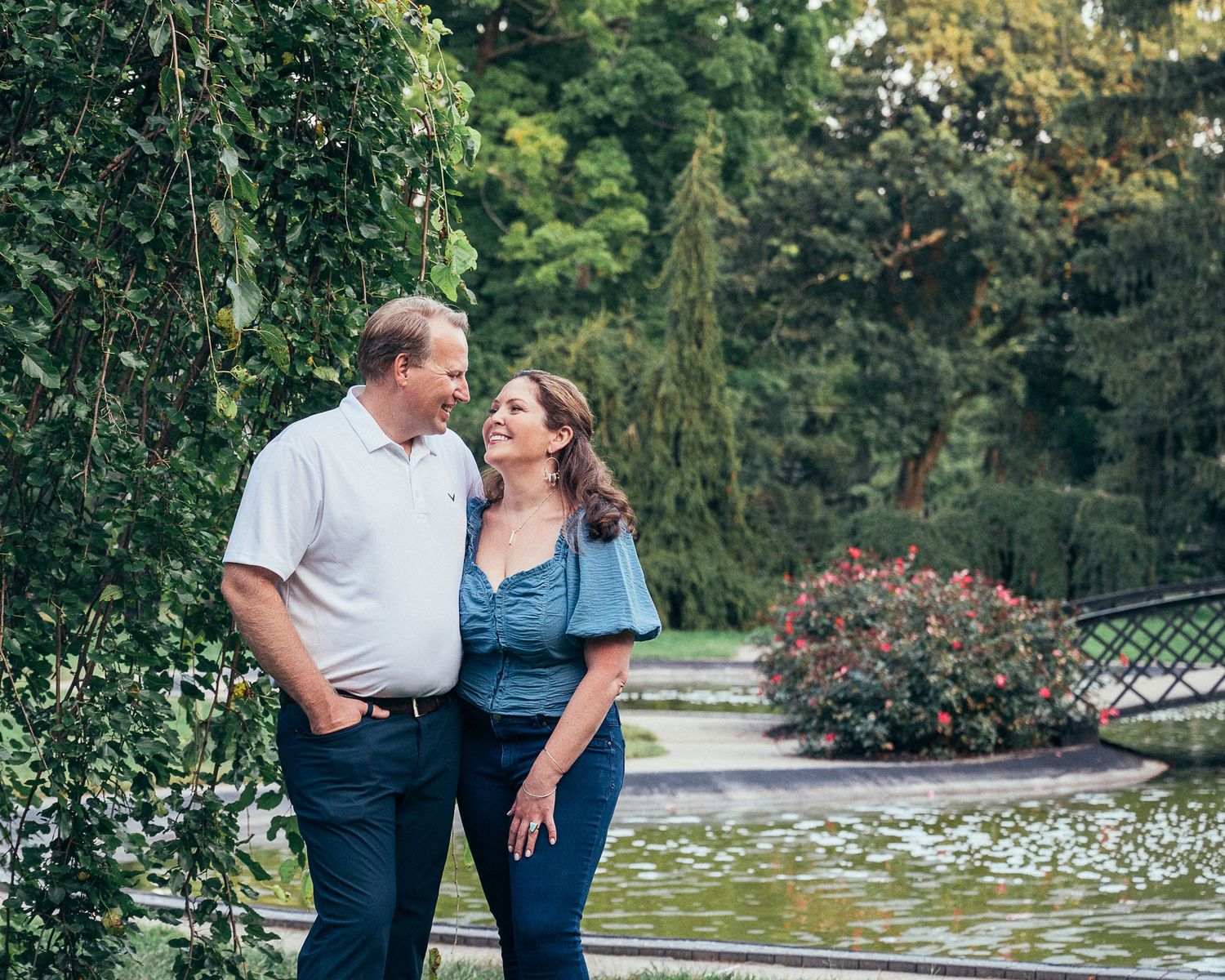 Couple in casual attire sharing romantic moments together in a lush garden setting with blooming flowers and trees.