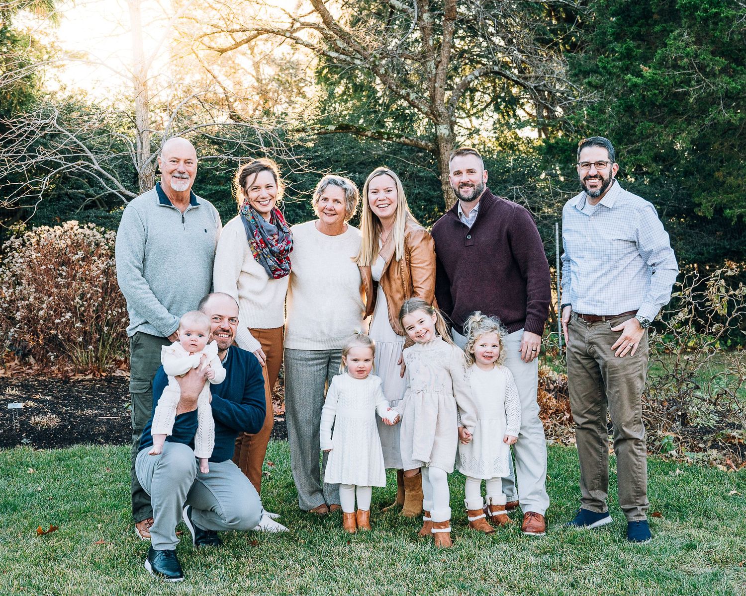 Large family gathering poses casually on grassy slope during autumn photoshoot wearing coordinated white and neutral outfits.