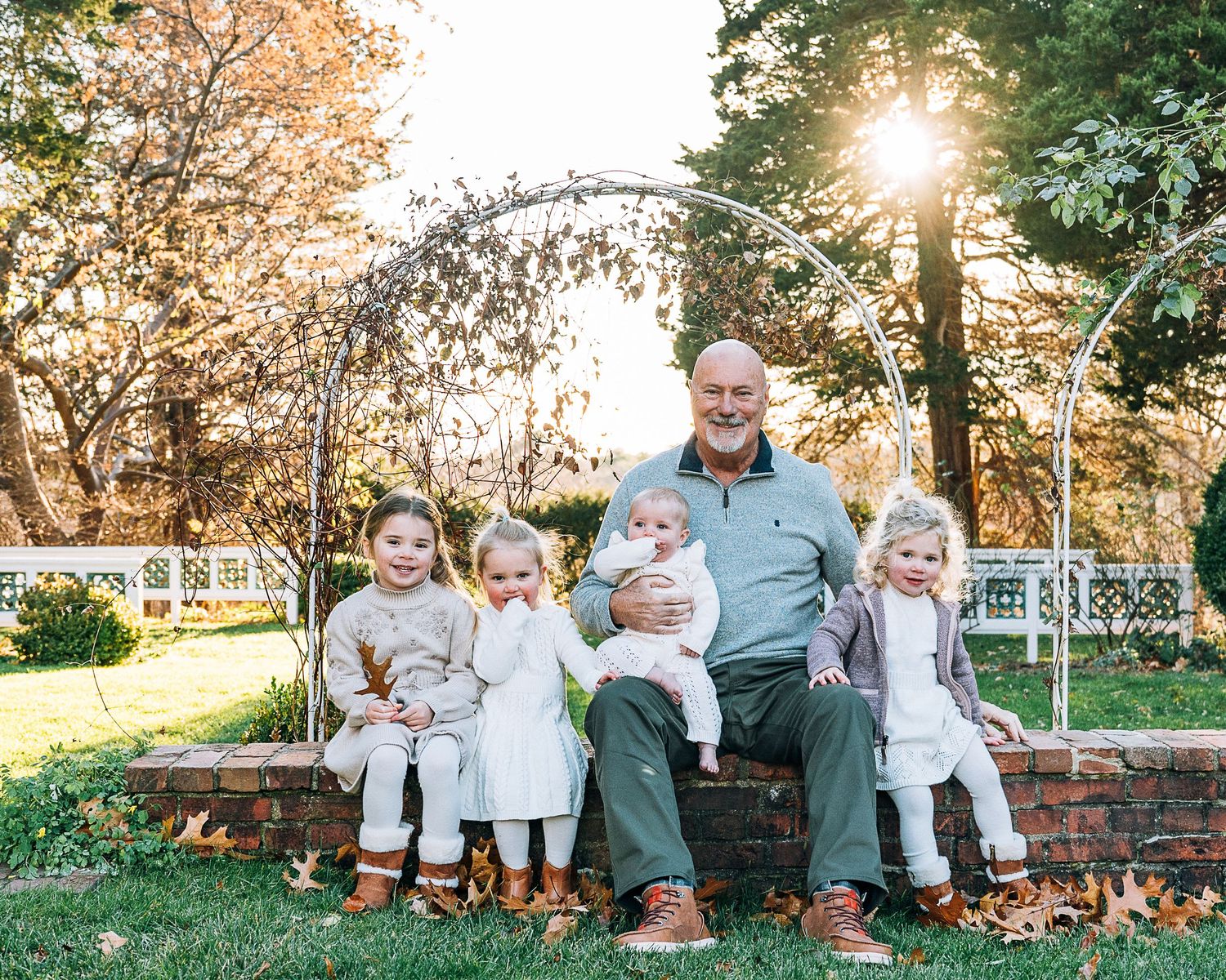 Family portrait session in a park during golden hour, showcasing five people on a rustic stone wall and bench.