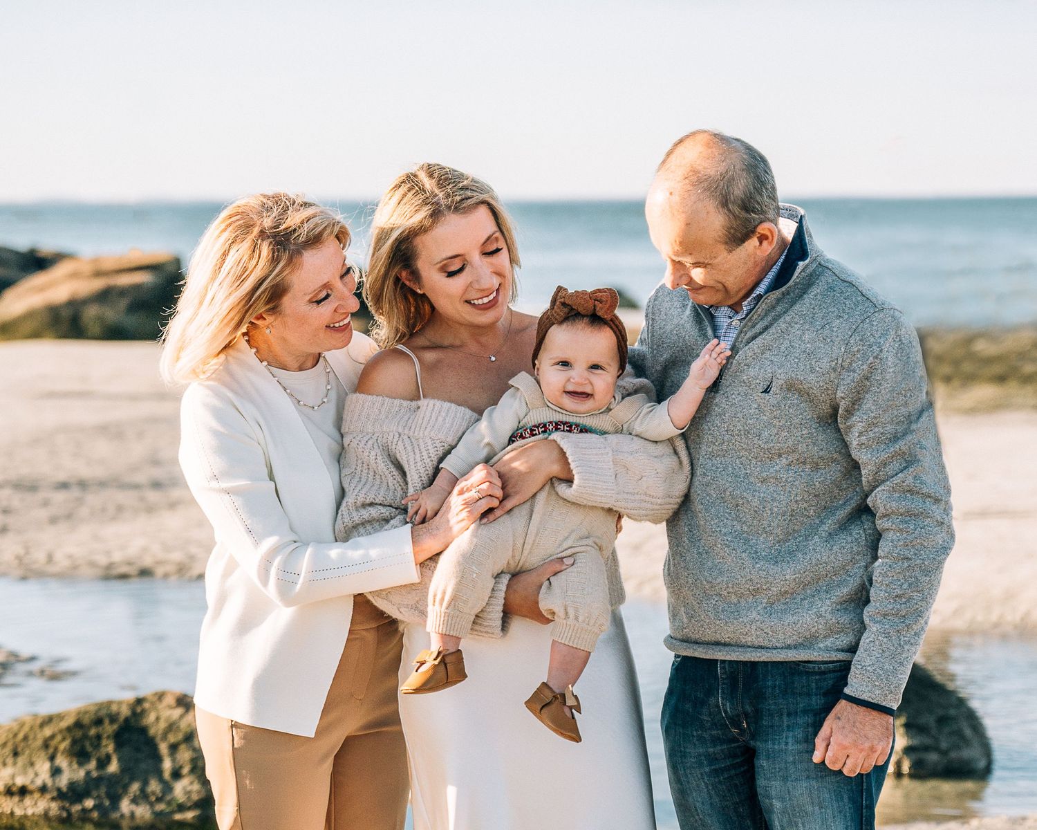 A happy family shares a tender moment together on a beach with rocks and ocean in the background.