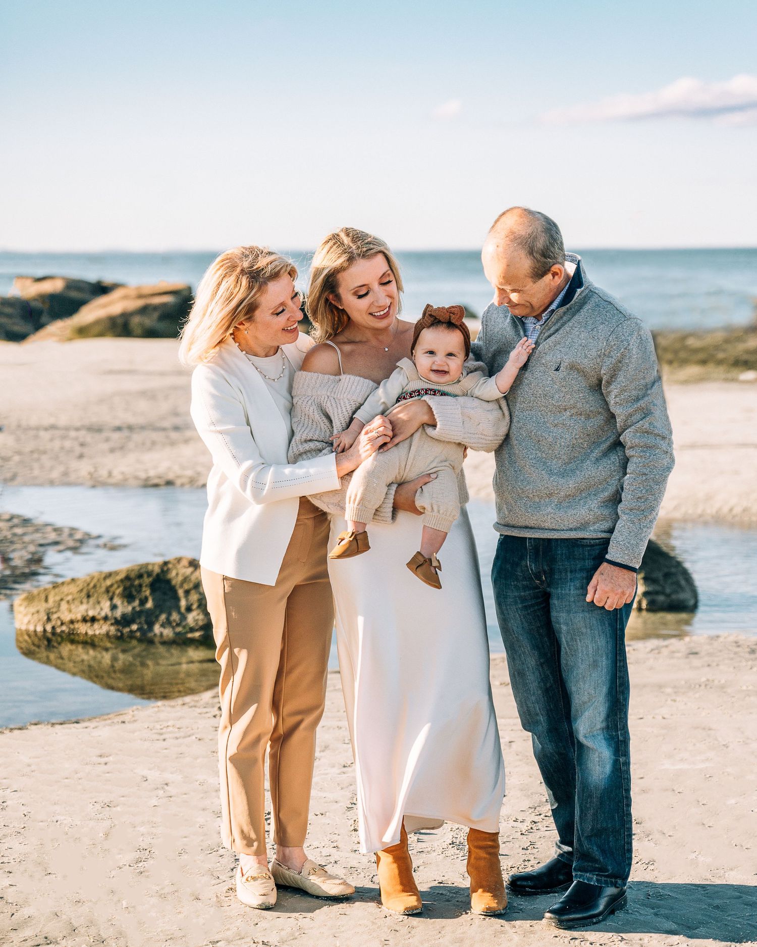 A loving family shares a joyful moment together on a rocky beach with the ocean and clear blue sky behind them.
