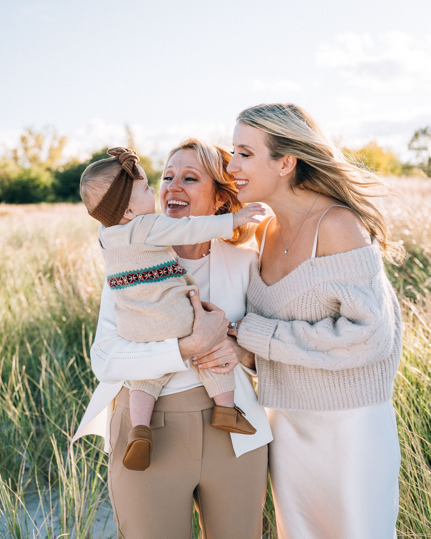 Three people sharing a joyful moment together while standing in a sun-lit field with tall grass during golden hour.