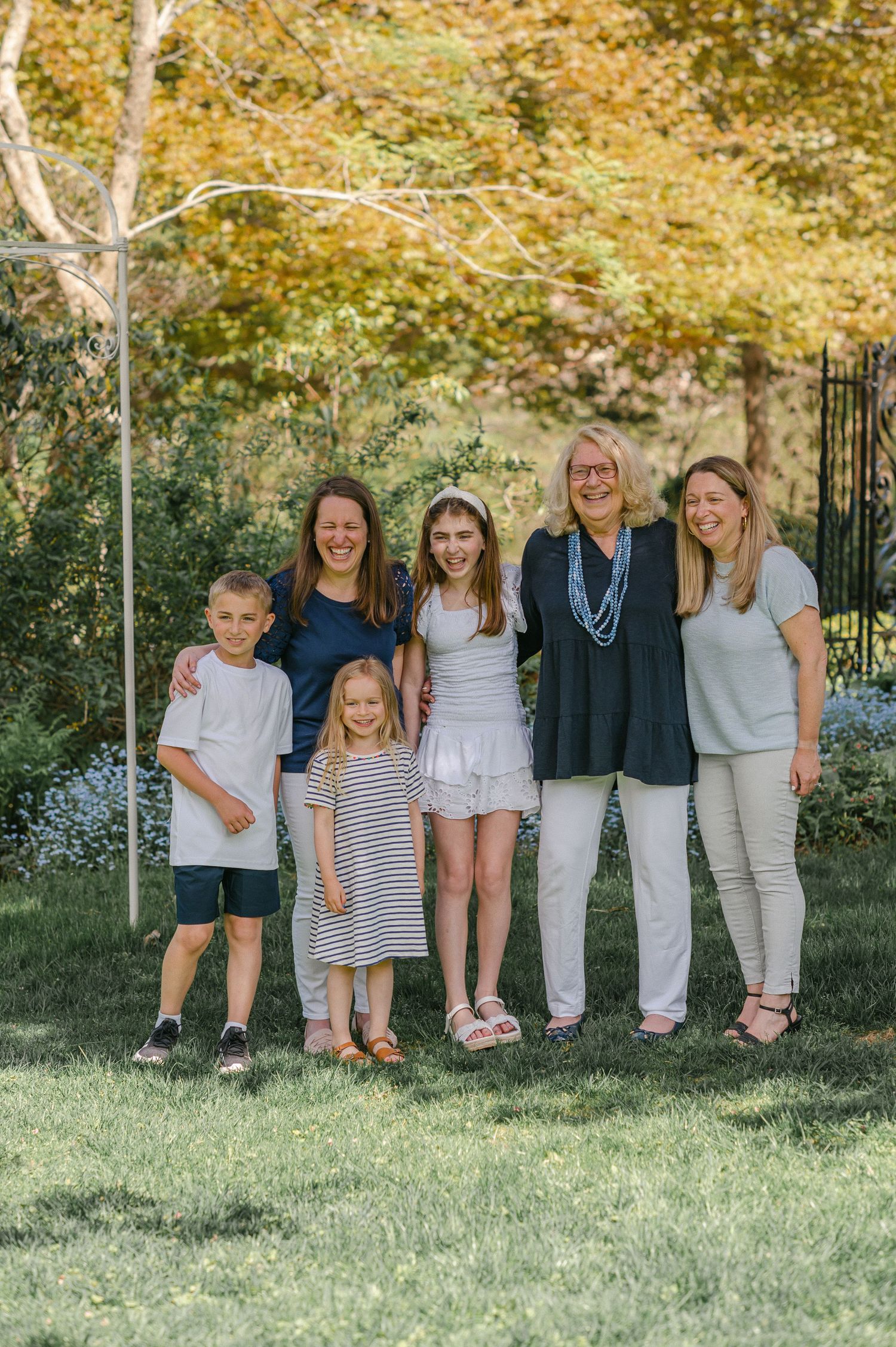 Family group wearing coordinated blue and white casual outfits sitting together on grass in outdoor garden setting.