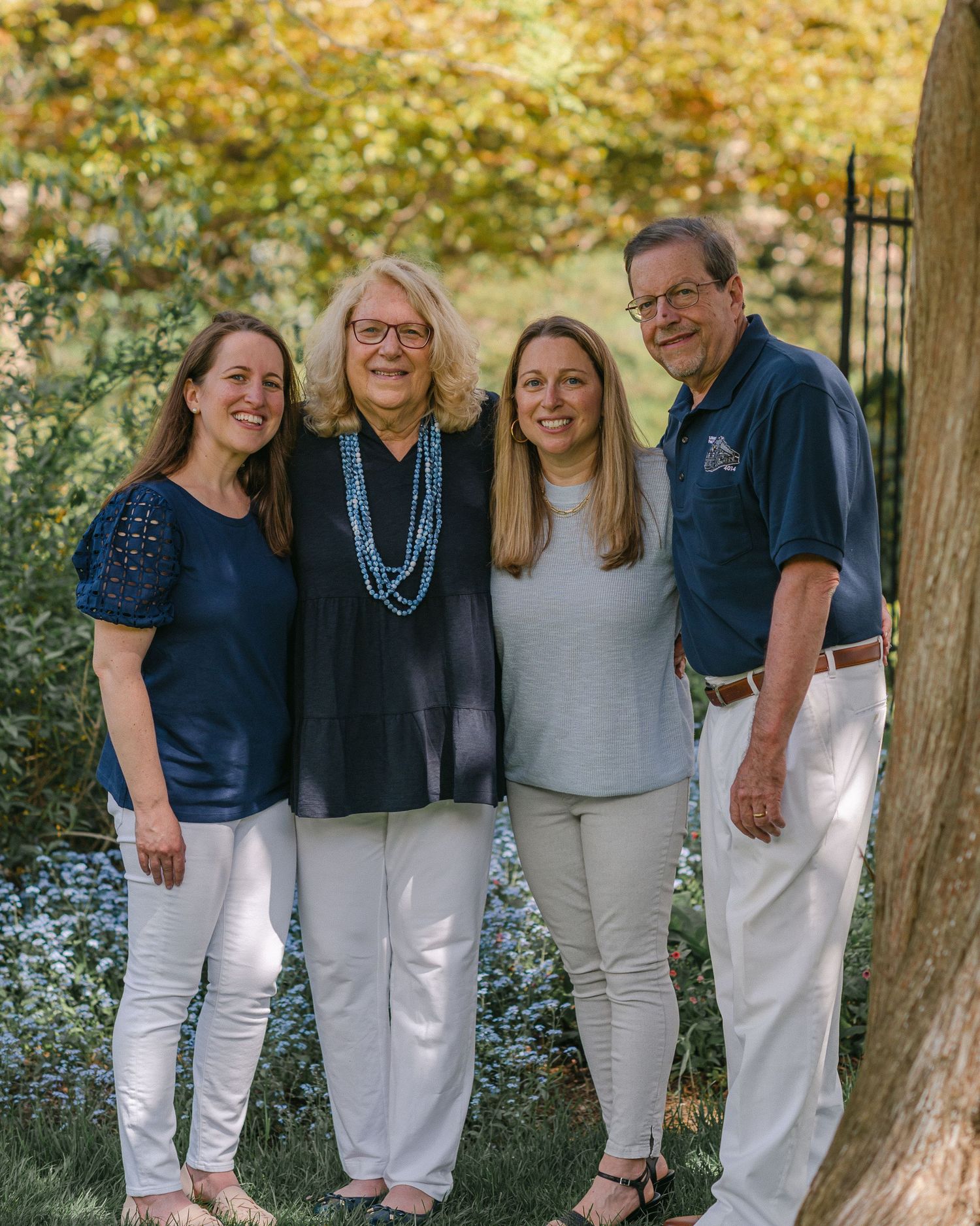 A family group stands together outdoors on a fall day wearing coordinating navy and white outfits.