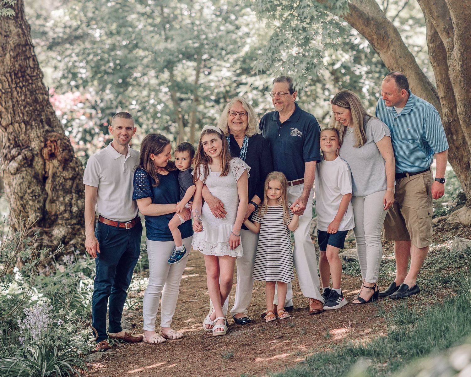A group stands together in a wooded outdoor setting wearing coordinated casual outfits in light neutral colors.