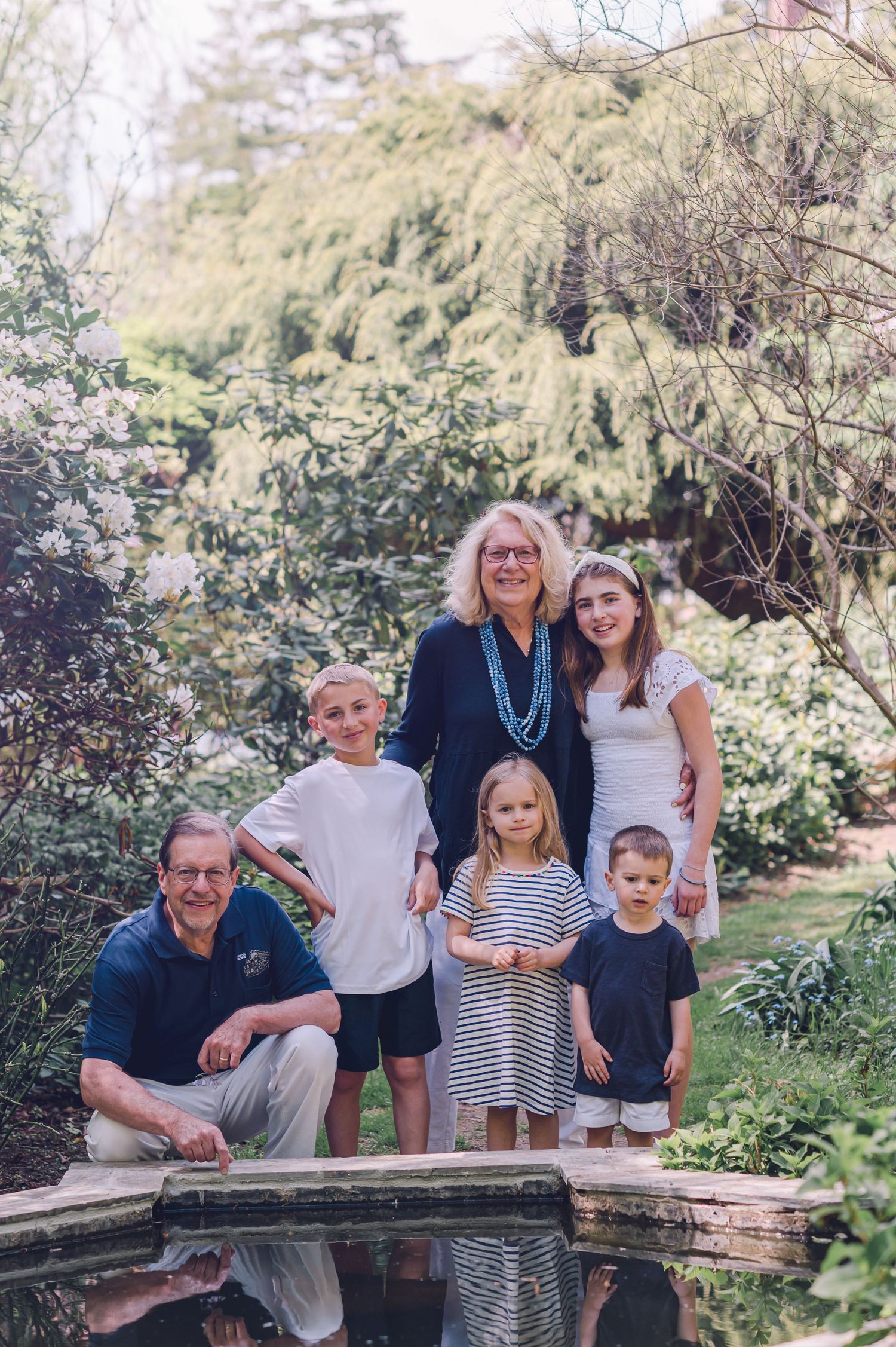 Multi-generational family poses together near a reflective pond in a lush garden setting.
