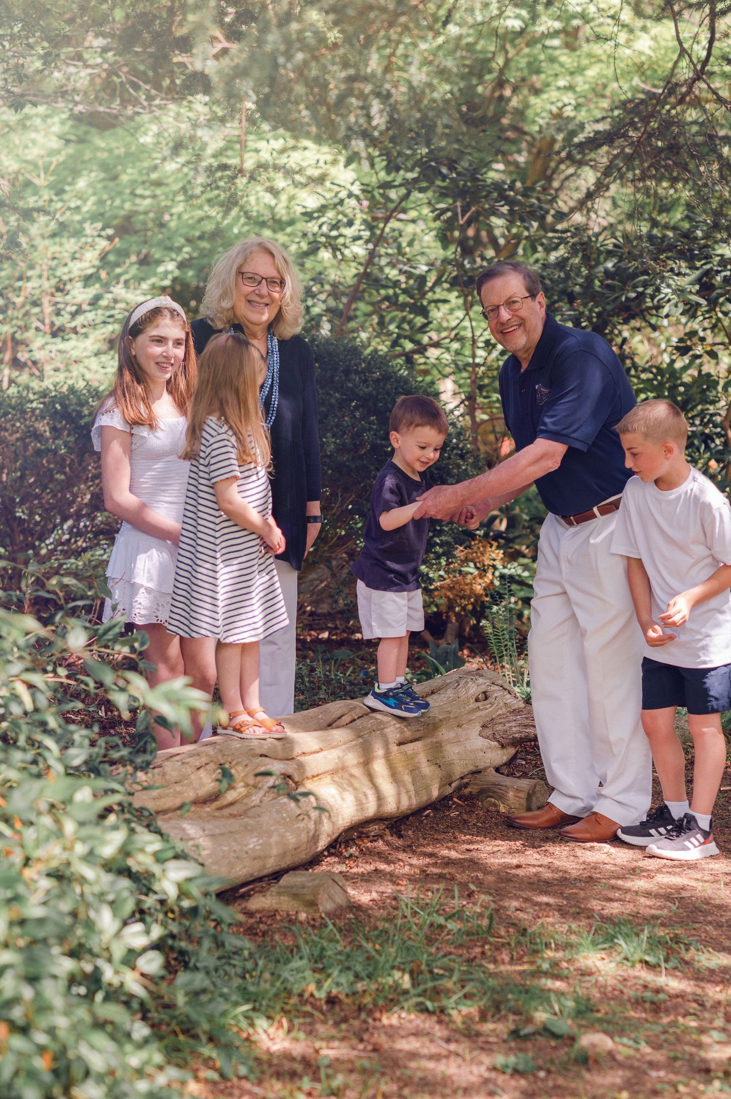 A family group enjoying time together on a fallen log trail in a wooded forest setting on a sunny day.