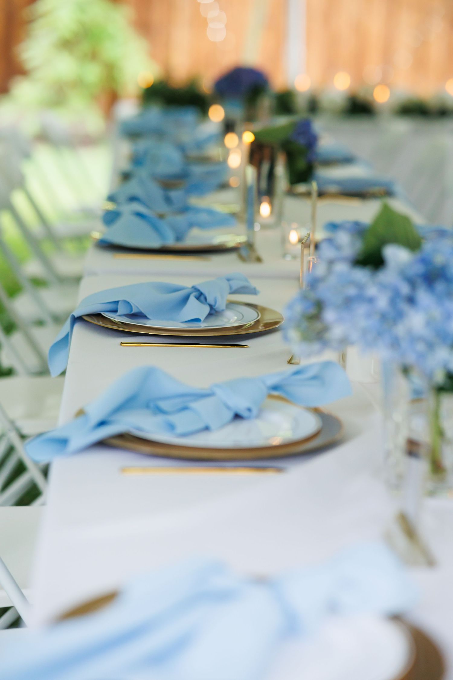 An elegant table setting features light blue napkins and white plates with delicate floral accents and glassware. Wedding photography dallas