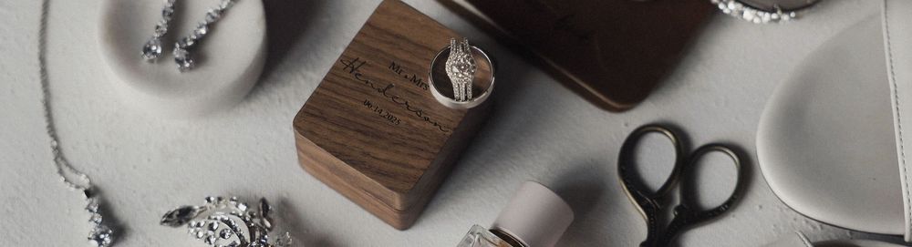 Dark and light minimalist flatlay of wooden jewelry box, scissors, and rings on a white surface.